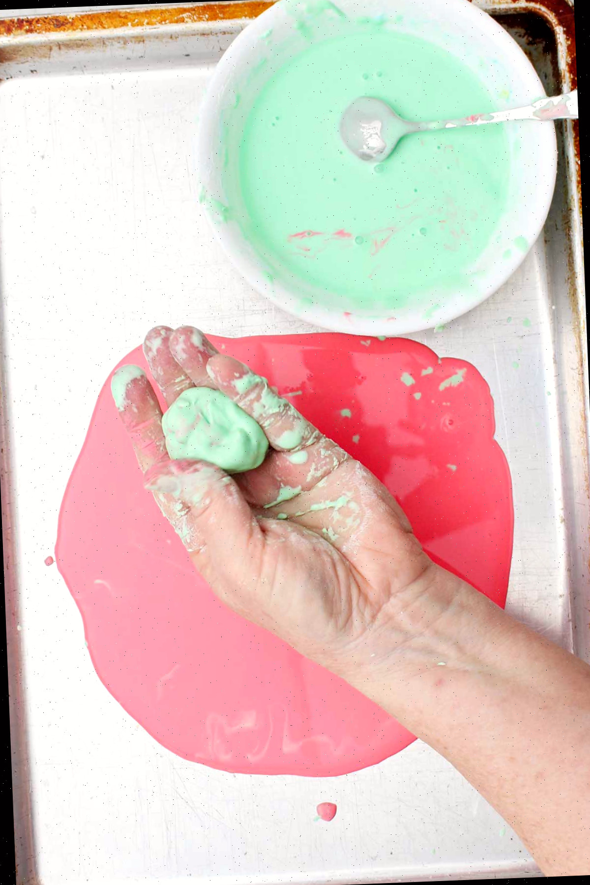 Uma pessoa segurando uma bola de oobleck verde claro sobre uma assadeira.
