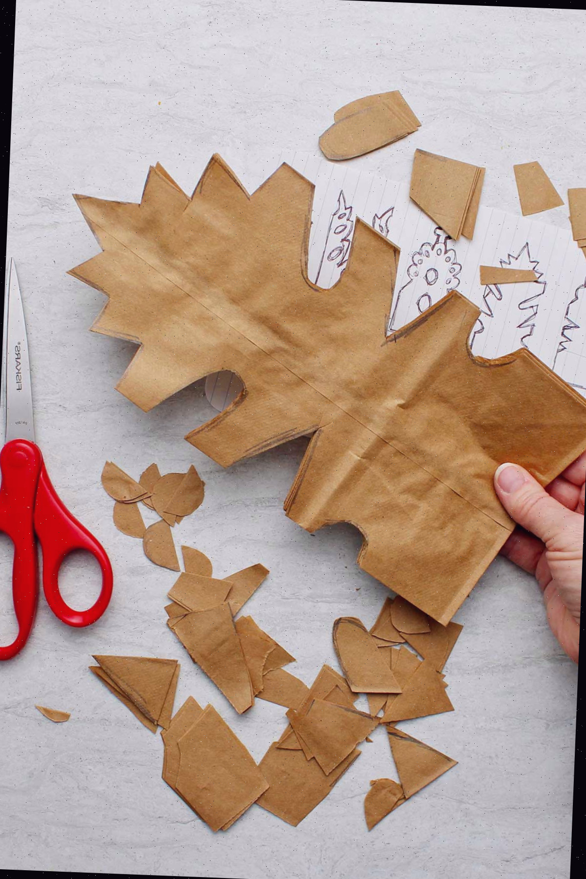 Mão segurando uma pilha de sacos de papel marrons dobrados após ter cortado o padrão.
