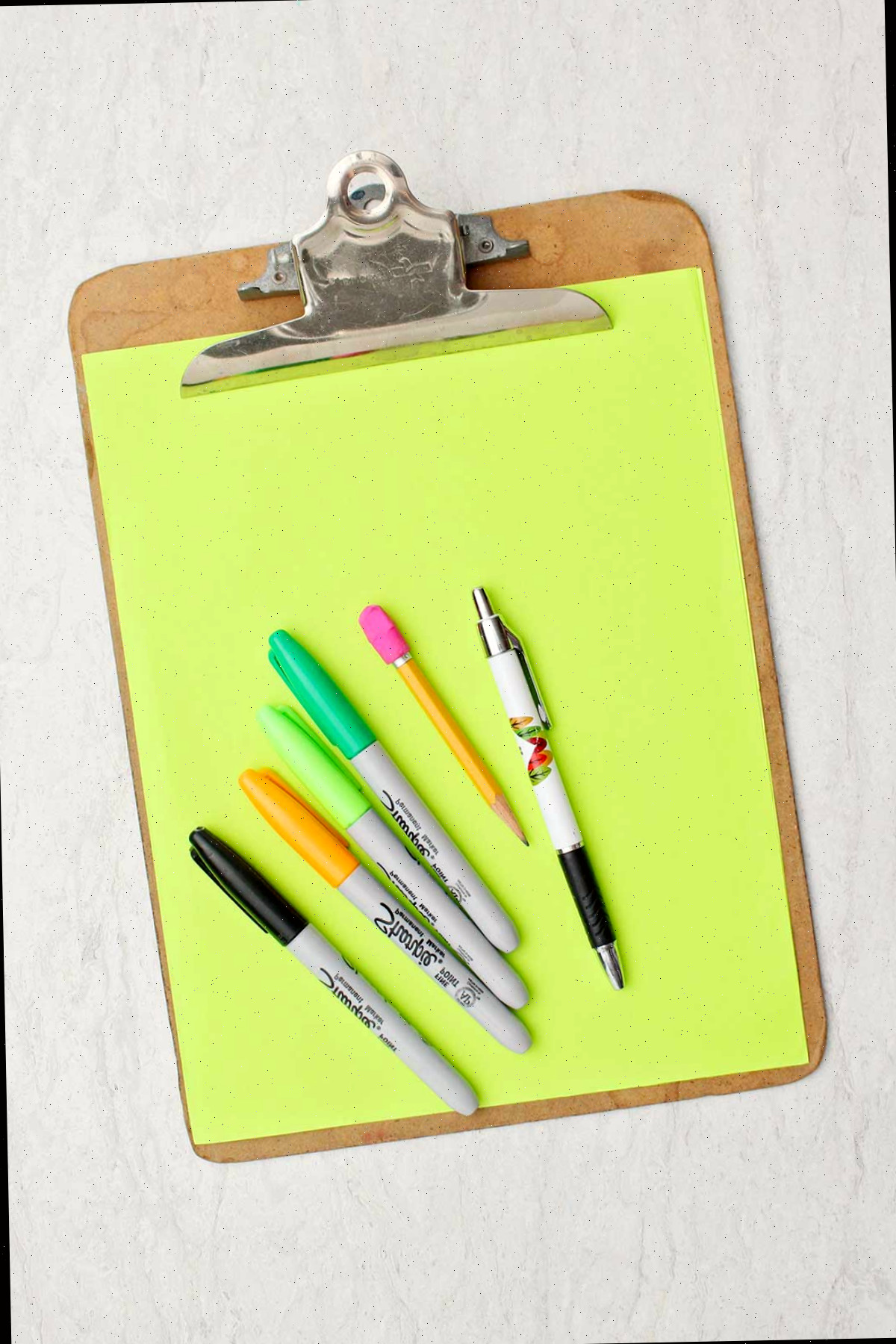 Um pedaço de papel verde, lápis, caneta e marcadores de várias cores.