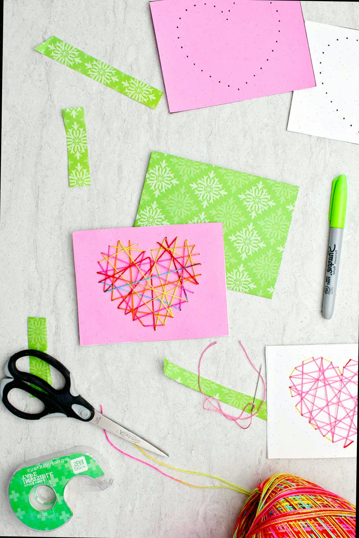 Dois cartões de Dia dos Namorados costurados feitos de papel rosa, branco e verde, com fio multicolorido e dois outros cartões com furos prontos para serem costurados.