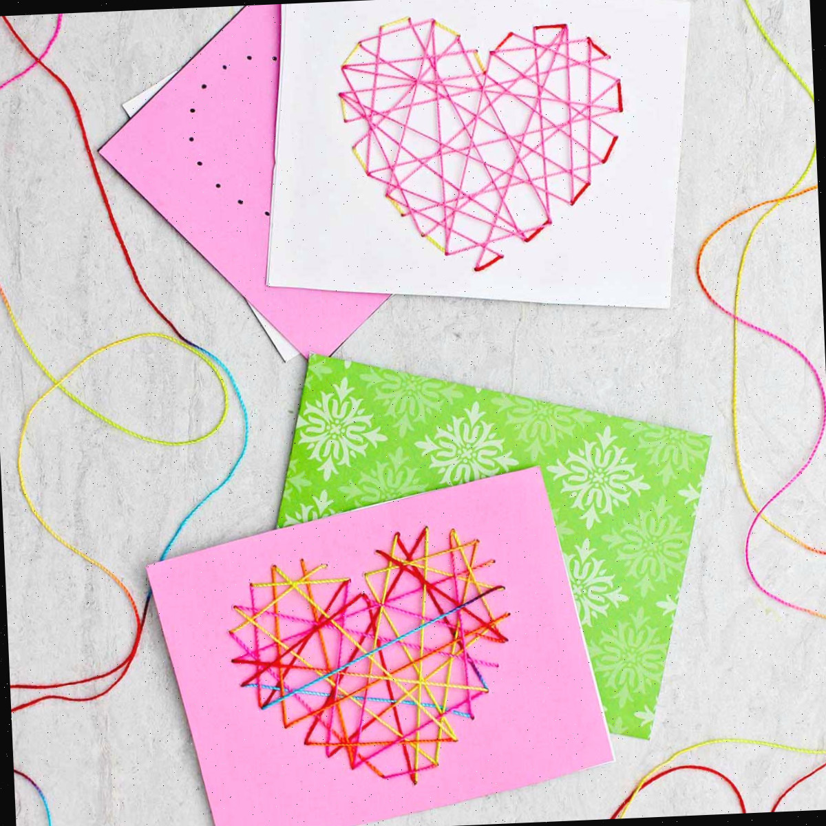 Dois cartões de dia dos namorados costurados feitos de papel rosa, branco e verde e fio multicolorido.