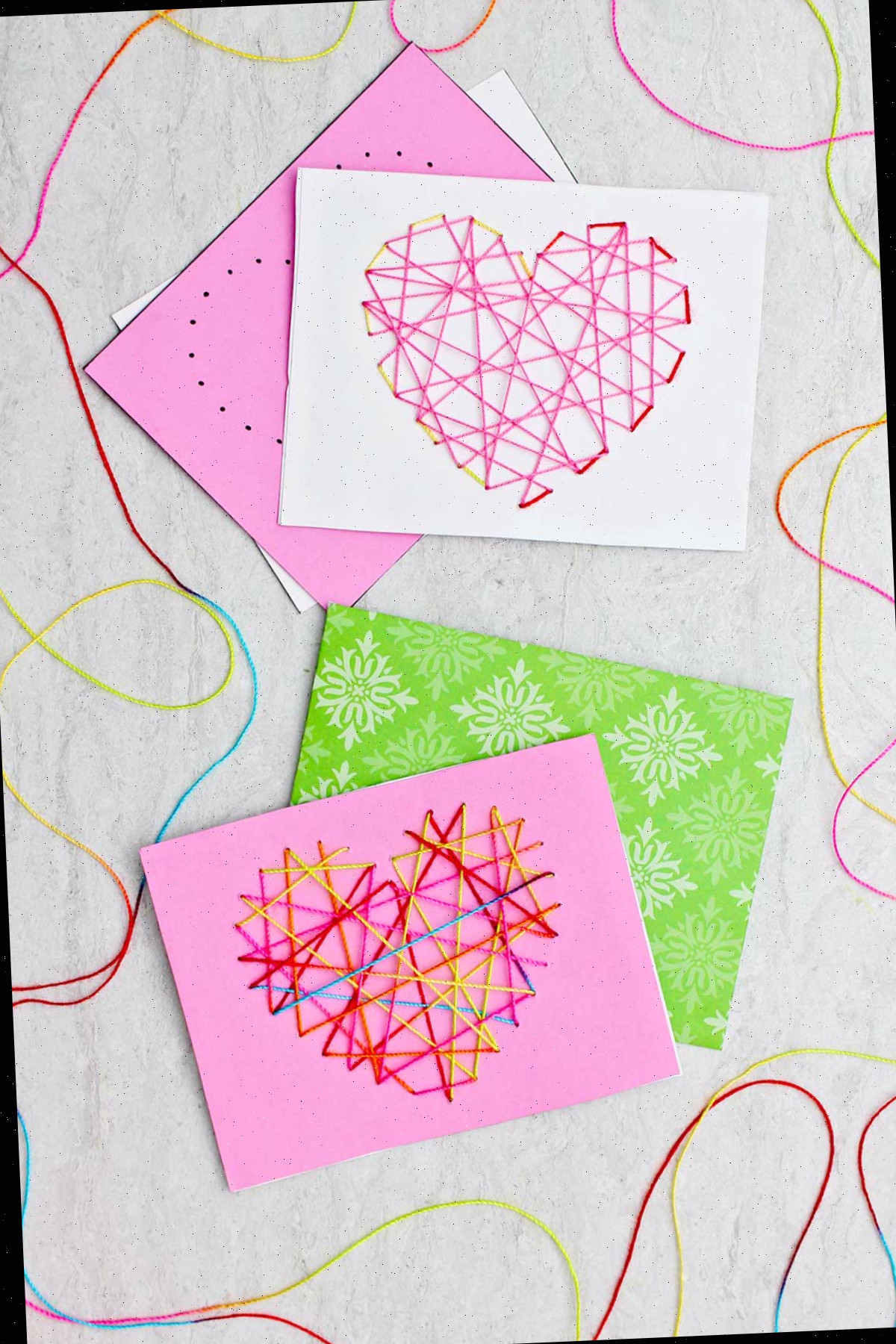 Dois cartões de Dia dos Namorados costurados feitos de papel rosa, branco e verde e linha colorida.