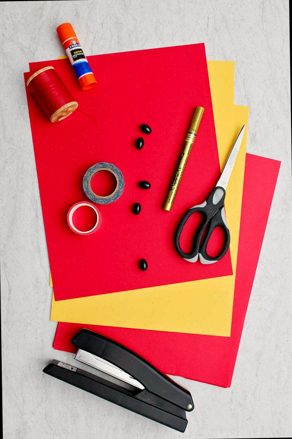 Materiais necessários para criar Lanternas Chinesas Simples. Papel vermelho e amarelo, tesoura, caneta dourada, fita, cordão, cola e grampeador.