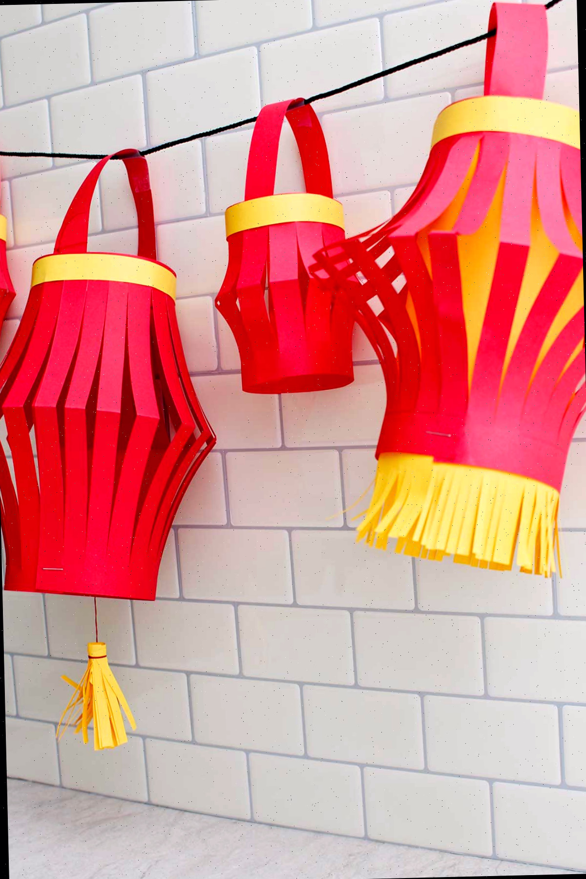 Quatro lanternas de papel completas penduradas contra um fundo de azulejos de metrô.
