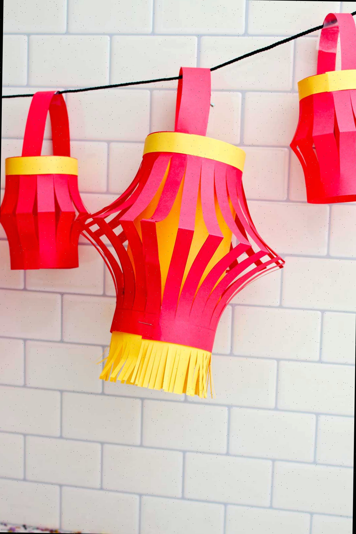 Três lanternas de papel completas penduradas contra um fundo de azulejos de metrô.