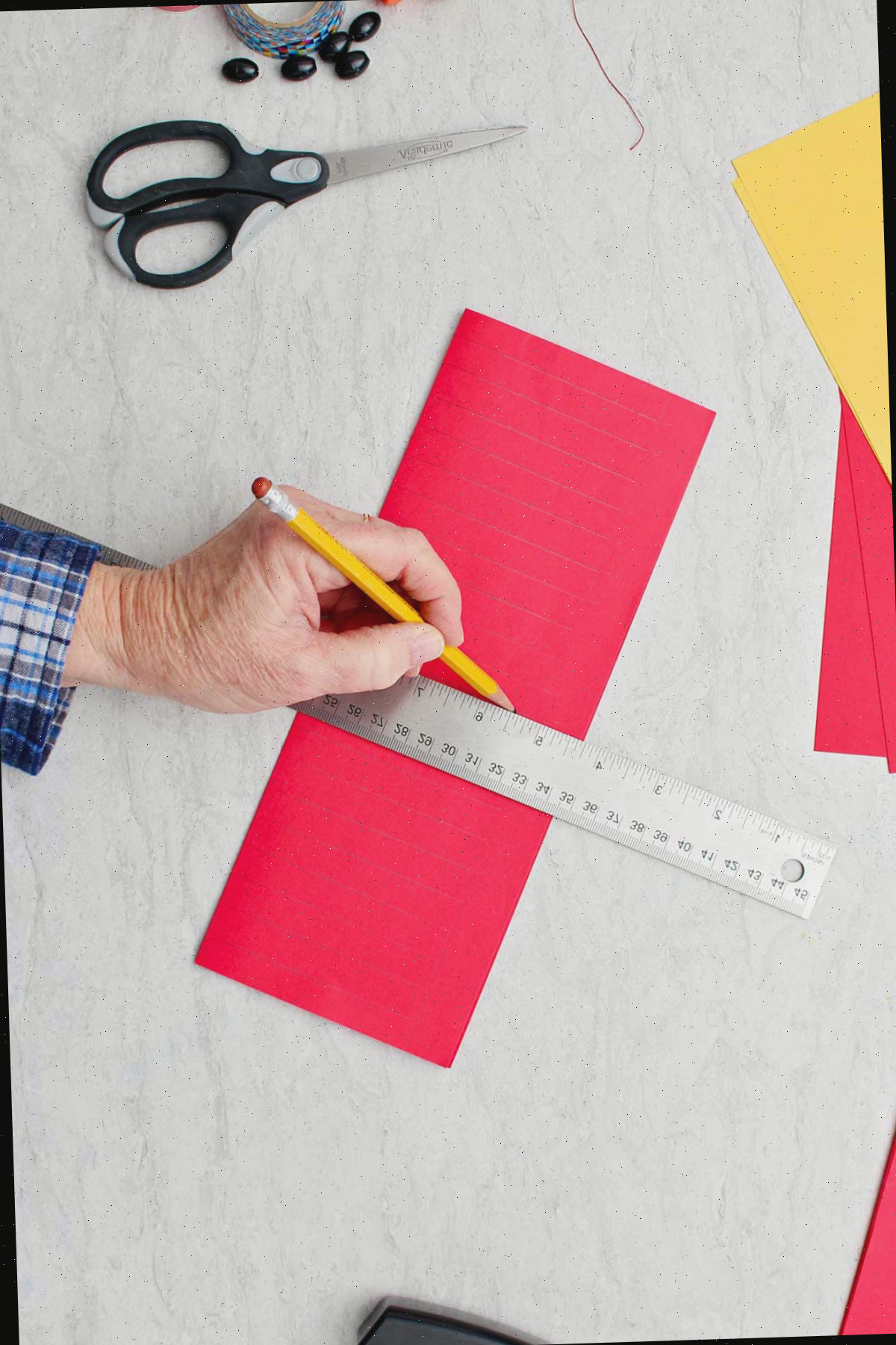 Desenhando linhas à mão com lápis em papel vermelho dobrado para fazer a base da lanterna.