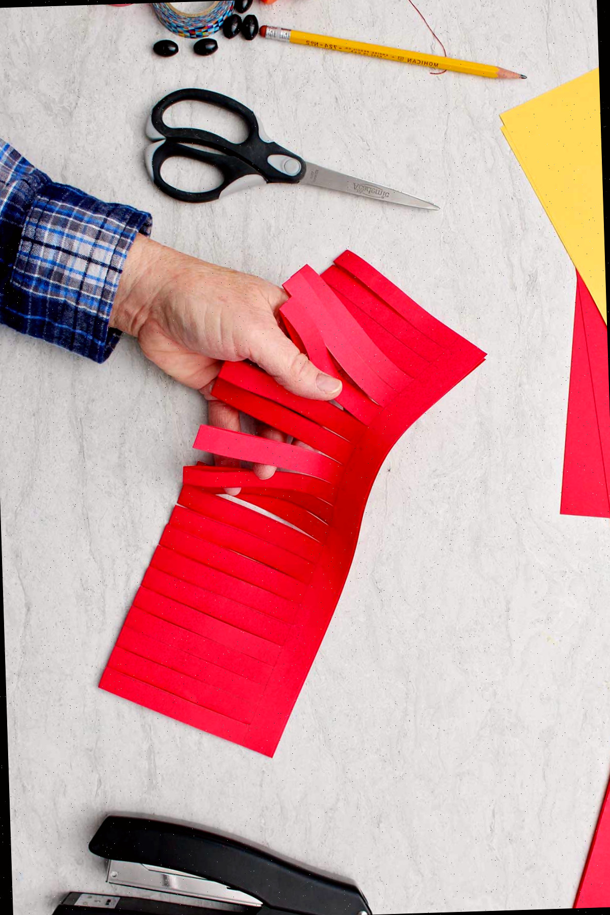 Mão mostrando pedaço de papel vermelho dobrado com tiras cortadas parcialmente para fazer a base da lanterna.