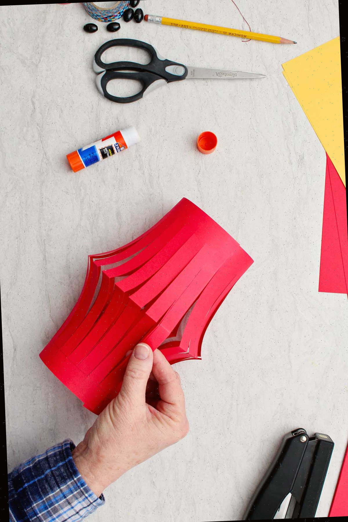 Mão mostrando a base da lanterna de papel vermelho com suprimentos ao redor.