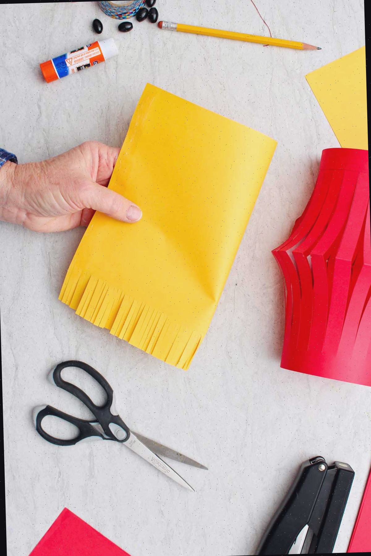 Mão mostrando um pedaço de papel amarelo com a parte inferior cortada em formato de franja.