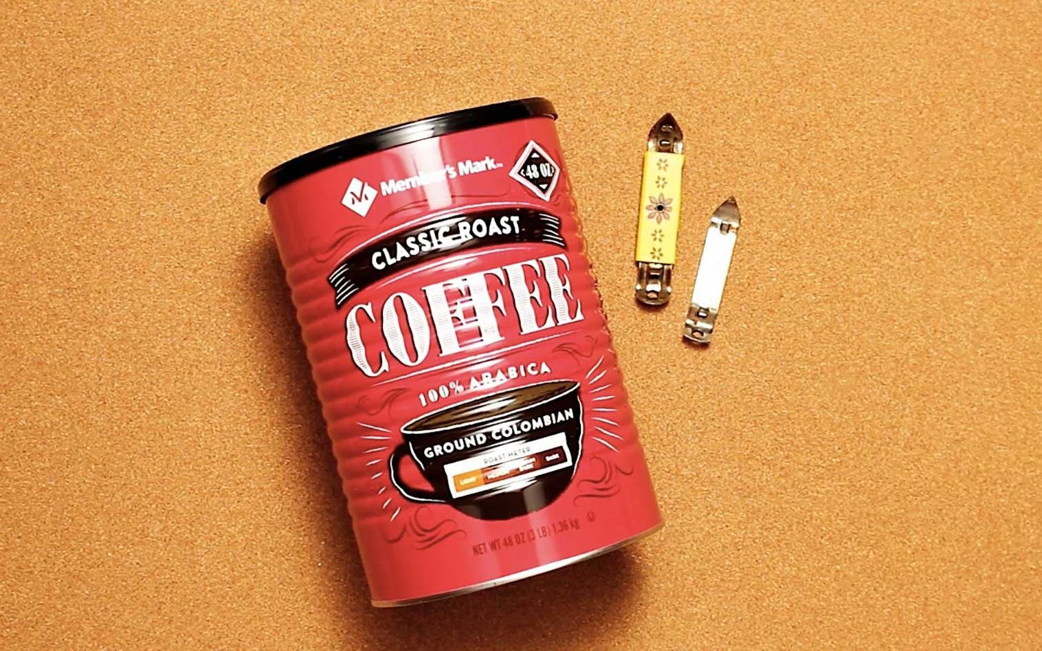 Dois pequenos abridores de lata e uma lata de café repousando sobre um fundo cor de cortiça.