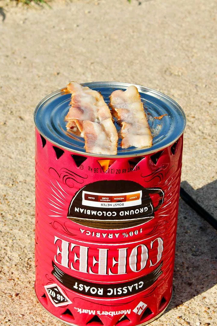 Pedaços de bacon prestes a serem cozidos em um fogareiro de pobre com um isqueiro laranja repousando na entrada da garagem.