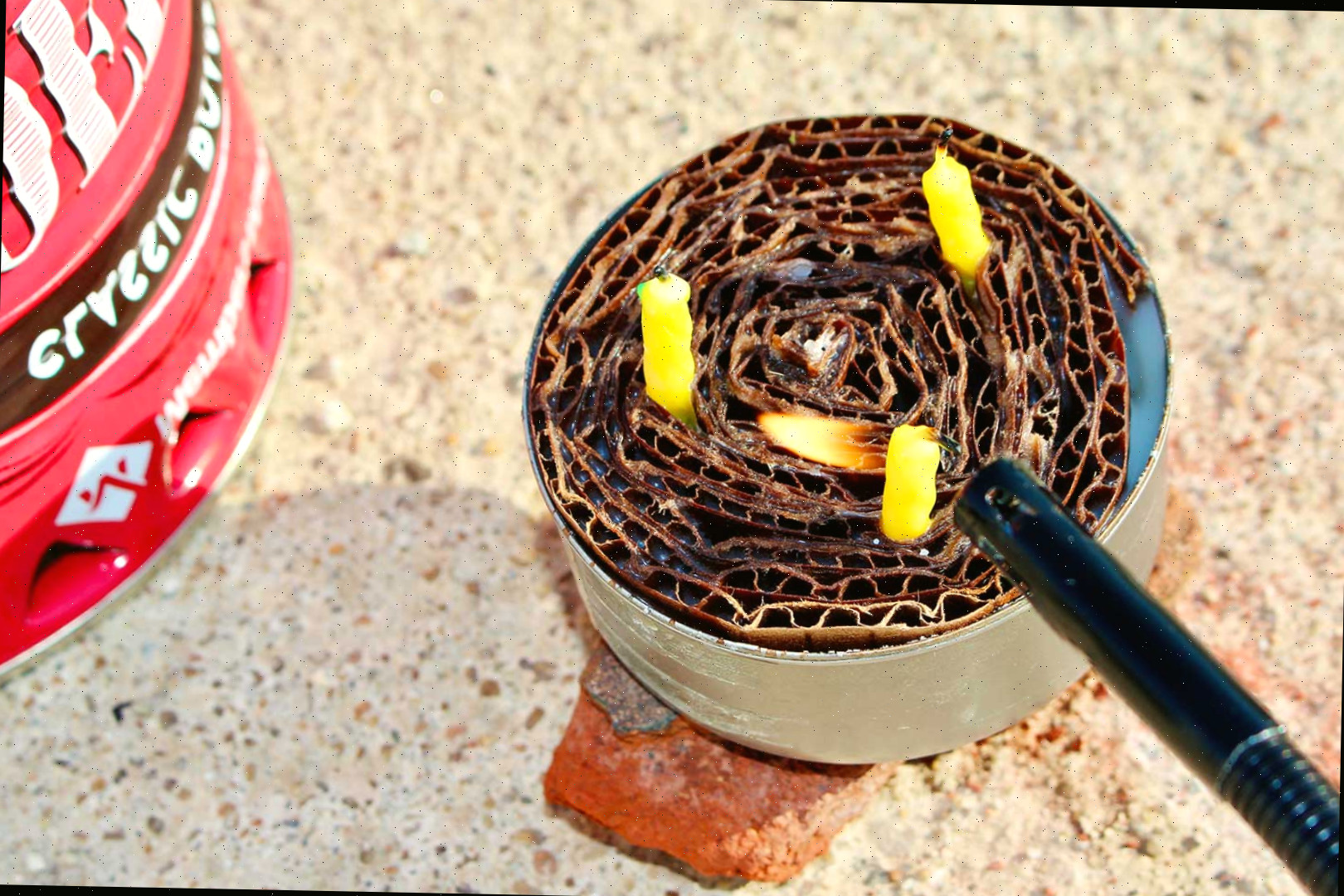 Alguém acendendo pequenas velas amarelas em um buddy burner de um fogareiro simples.