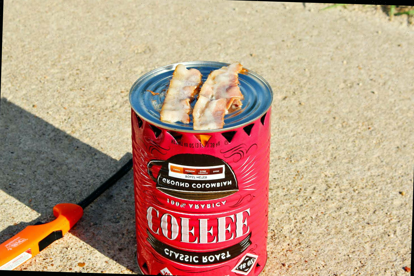Pedaços de bacon prestes a serem cozinhados em um fogareiro simples com um isqueiro laranja descansando na entrada da garagem.