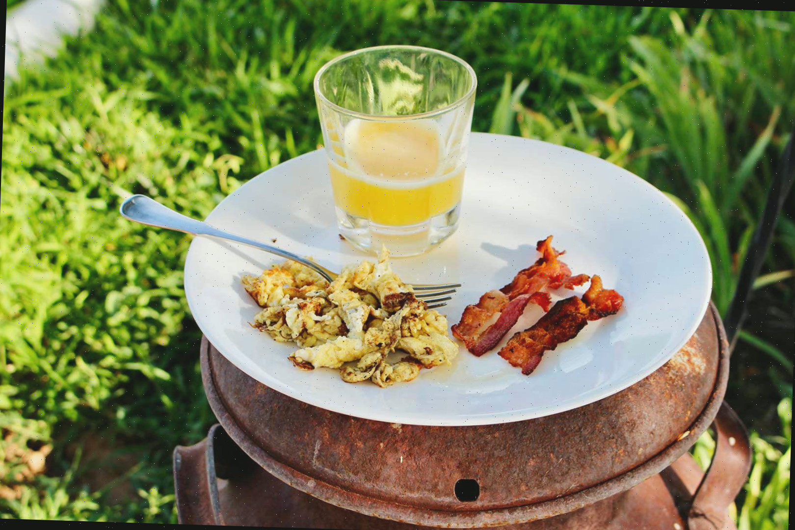 Um prato de bacon, ovos e suco no café da manhã pousado em cima de uma lata de óleo antiga.