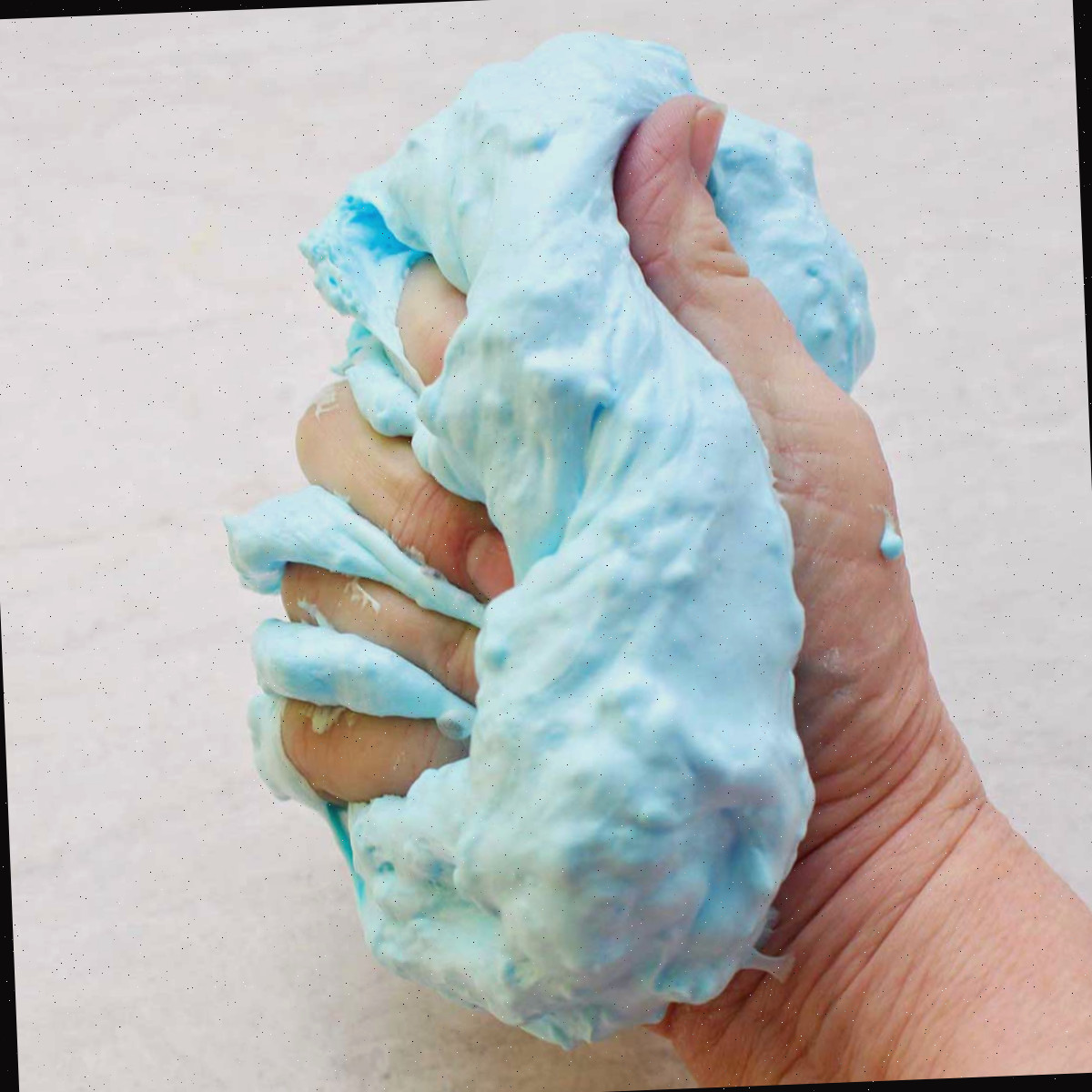 Mão apertando um lote pronto de slime fofo azul claro.