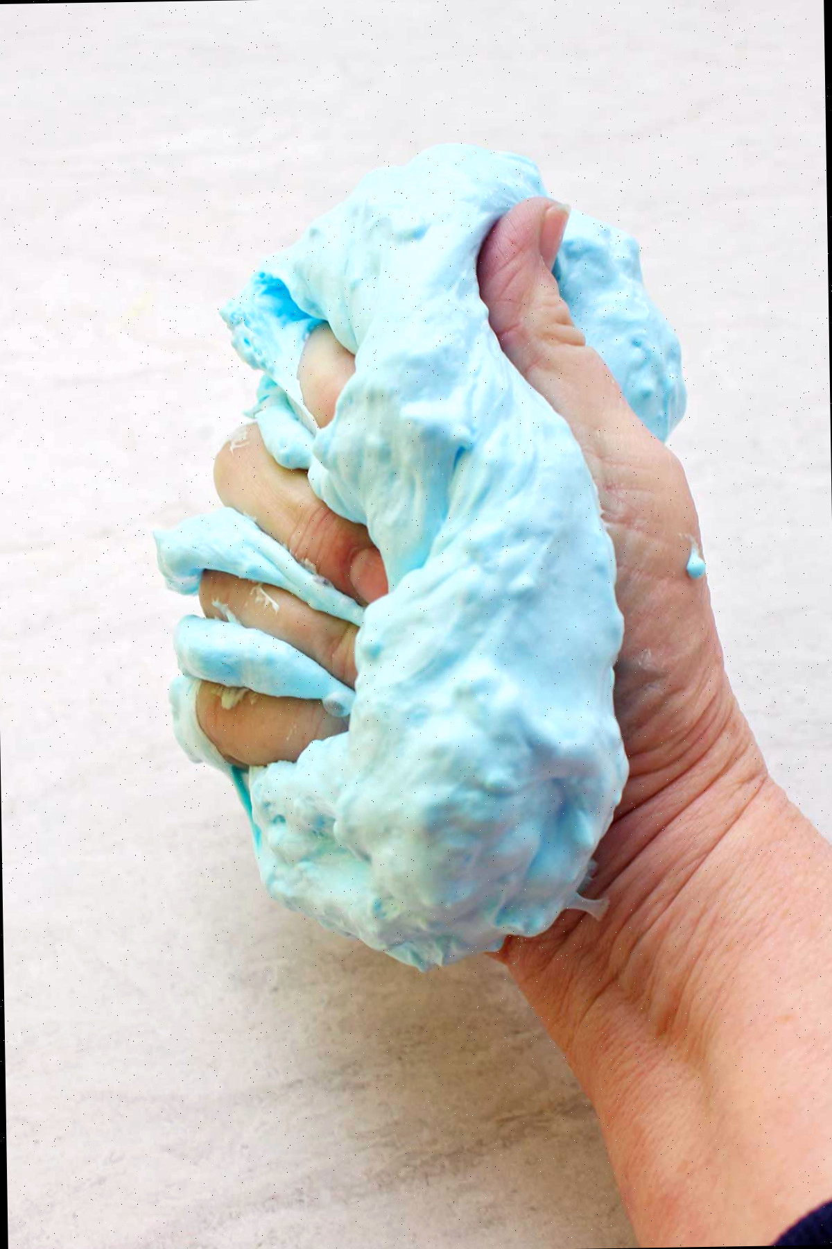 Mão pressionando um lote completo de slime fofinho de cor azul clara.