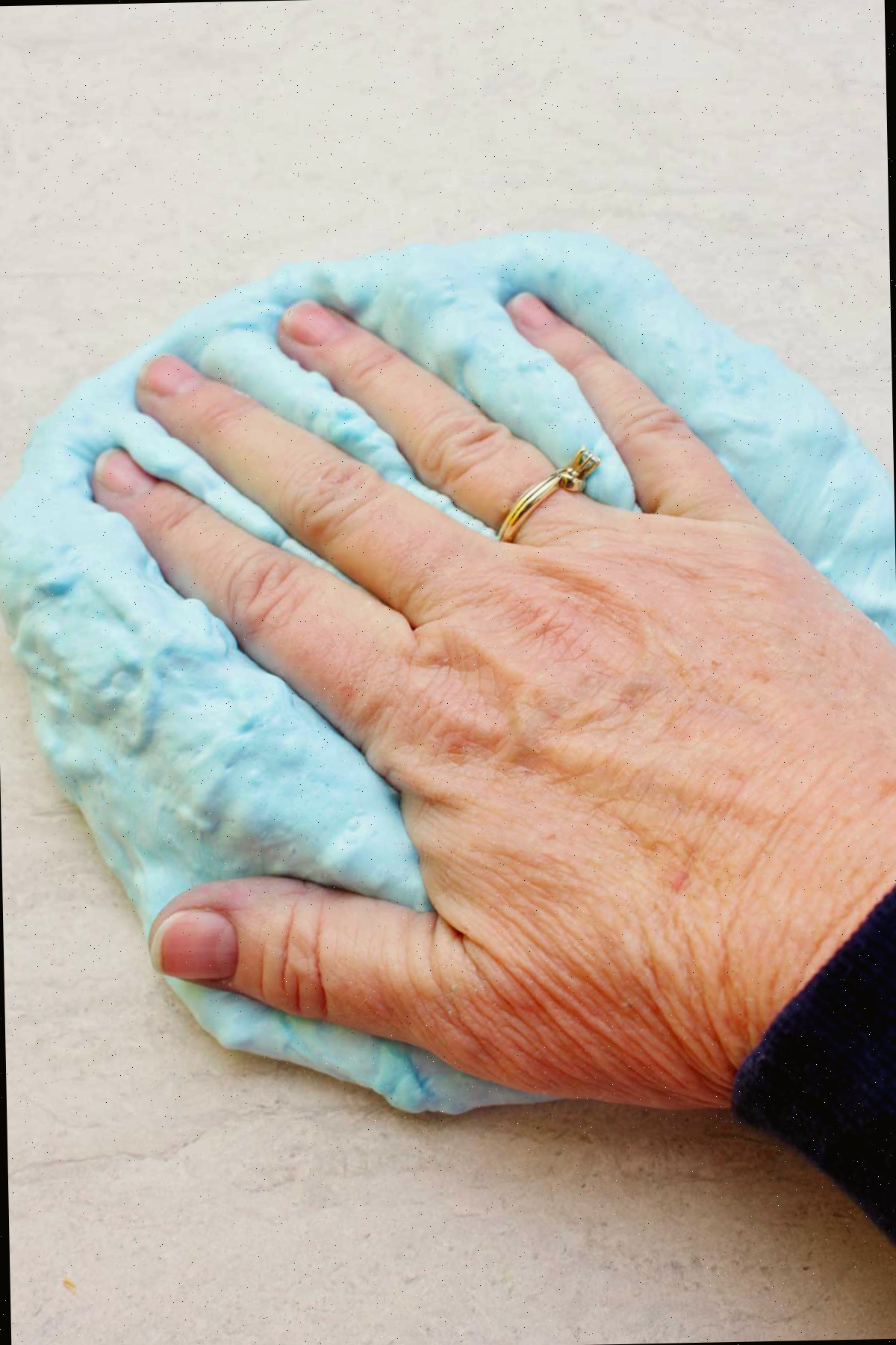 Mão pressionando uma porção de slime fofa azul clara já finalizada.