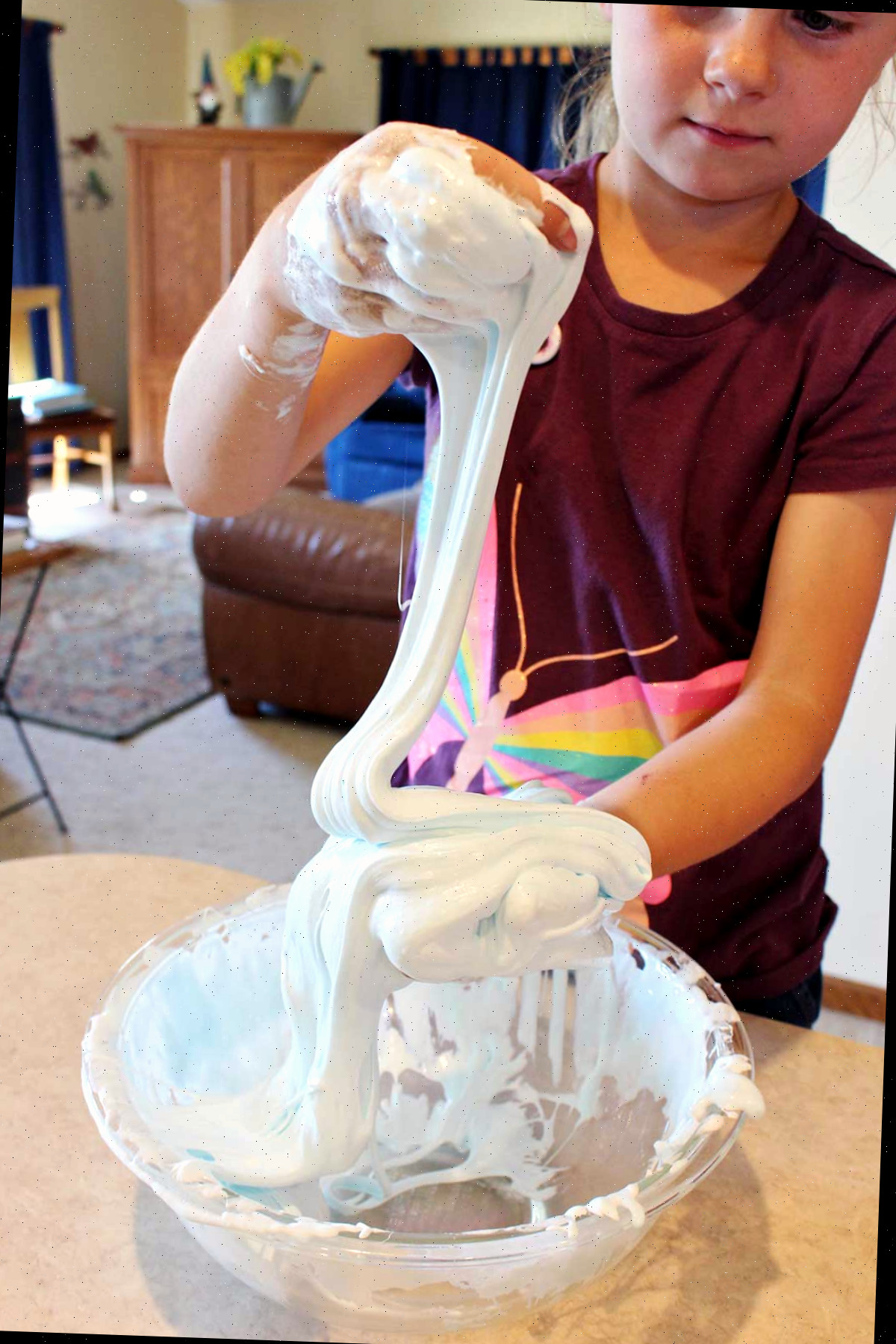 Menina jovem com camisa de borboleta marrom brincando com uma porção de slime fofa em uma tigela de vidro.