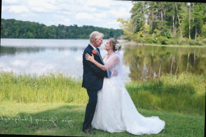 Casal mais velho em traje de casamento diante de um lago