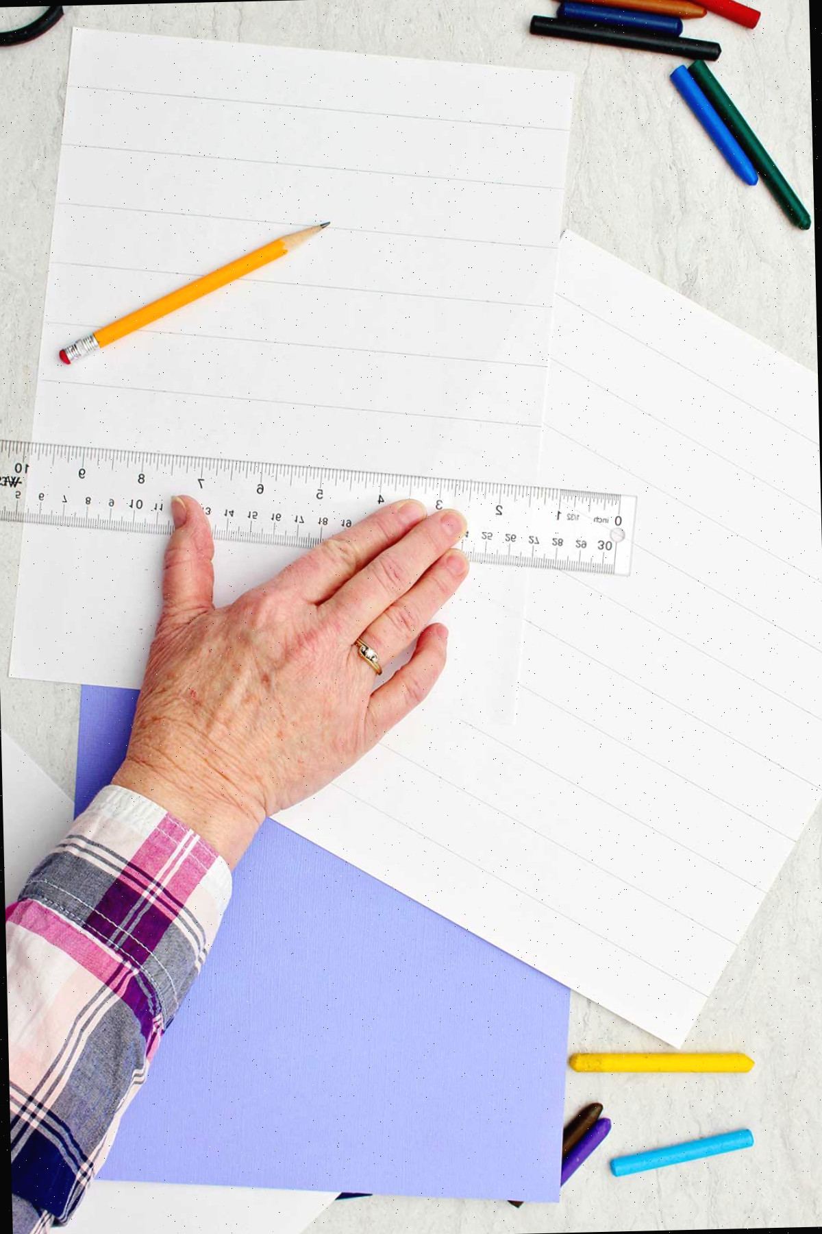 Pessoa desenhando tiras iguais em um pedaço de papel branco com uma régua e um lápis.