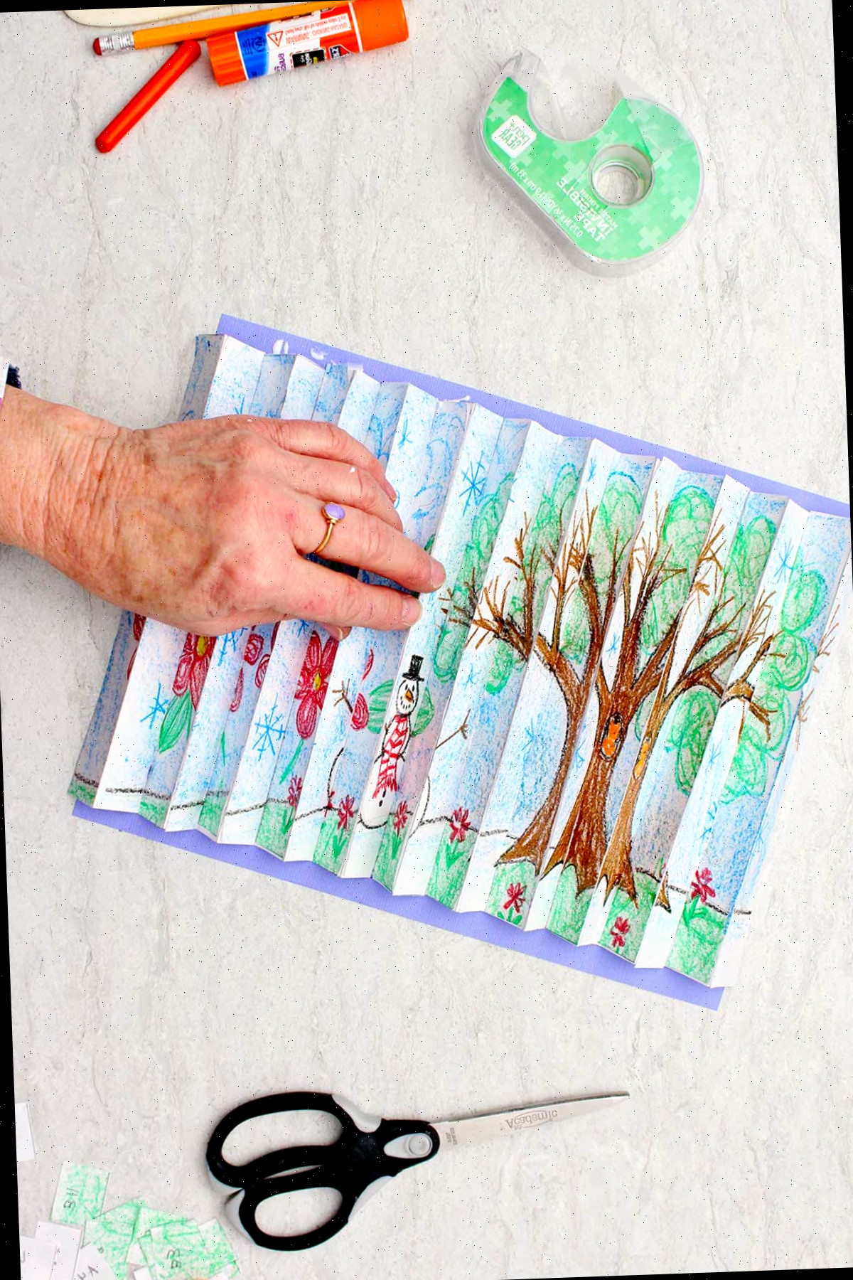 Indivíduo colando a imagem do agamógrafo completo de duas estações sobre um papel colorido azul.