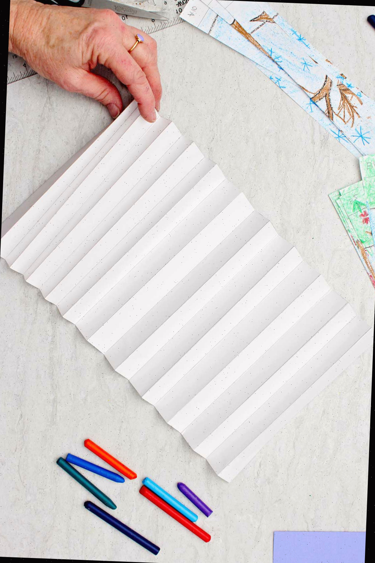 Indivíduo dobrando uma longa faixa de papel branco como um acordeão com outros materiais ao redor.