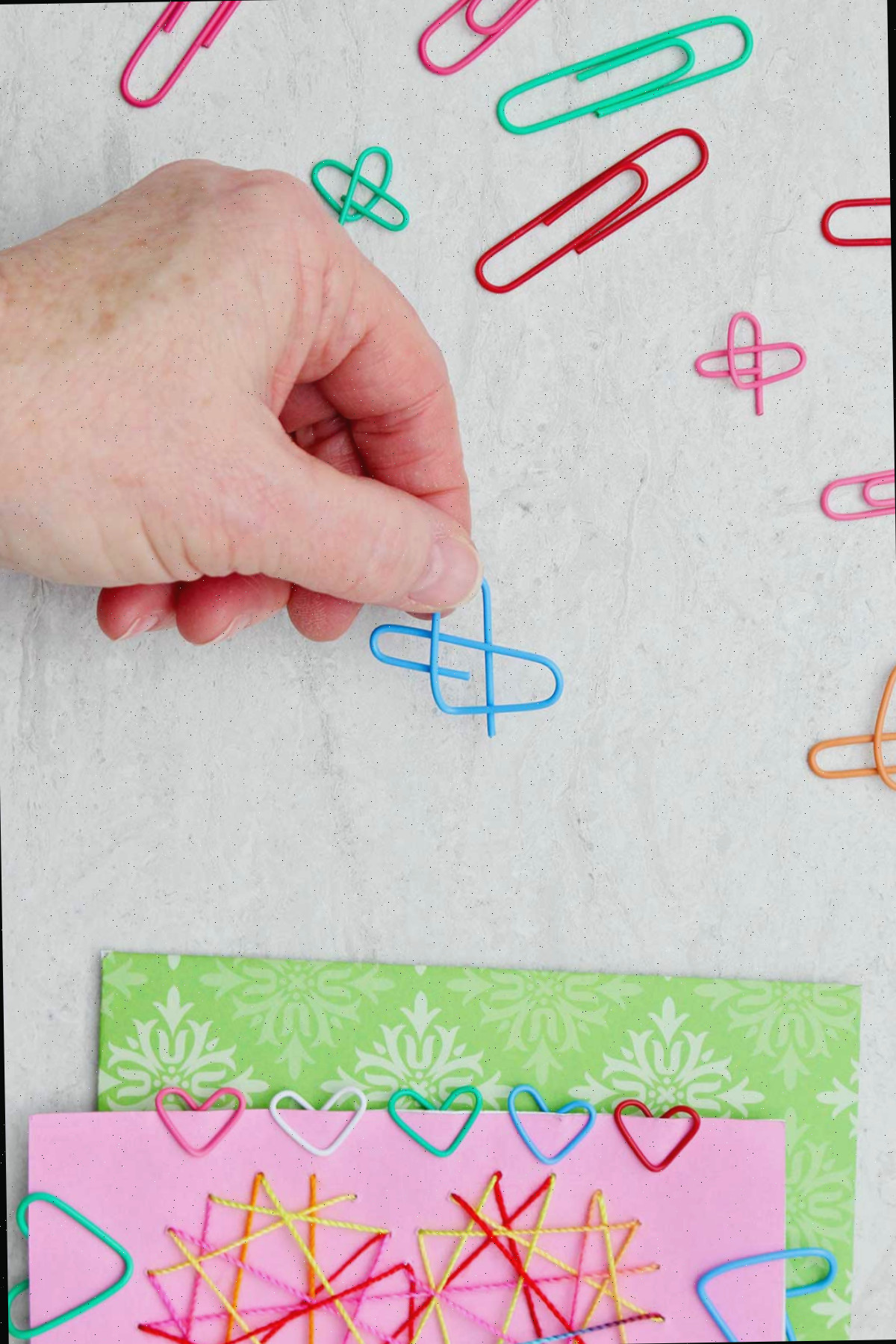 Pessoa segurando um clipe de papel azul dobrado em forma de coração com outros clipes de papel e um cartão de Dia dos Namorados próximos.