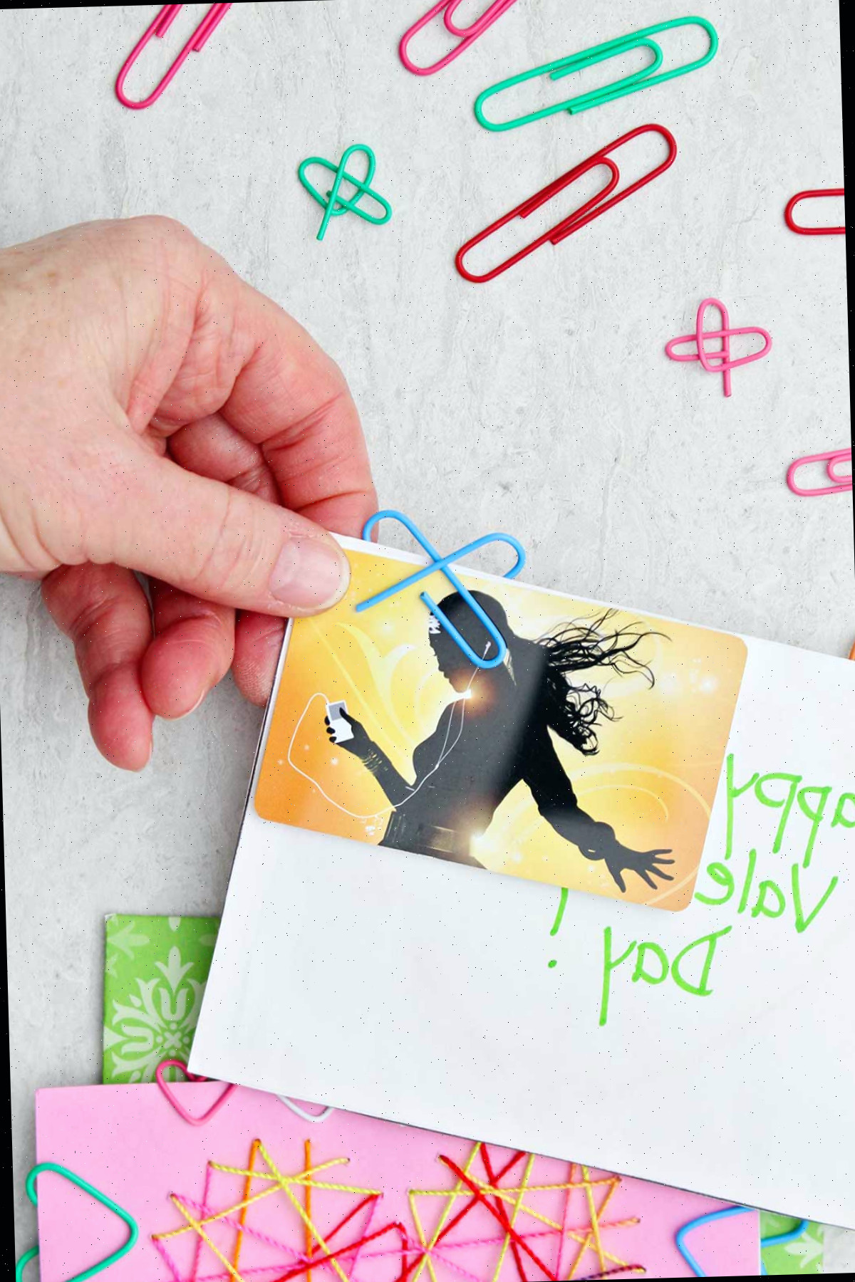 Uma pessoa mostrando o verso de um clipe de papel em forma de coração preso a um cartão de Dia dos Namorados com outros clipes de papel próximos.