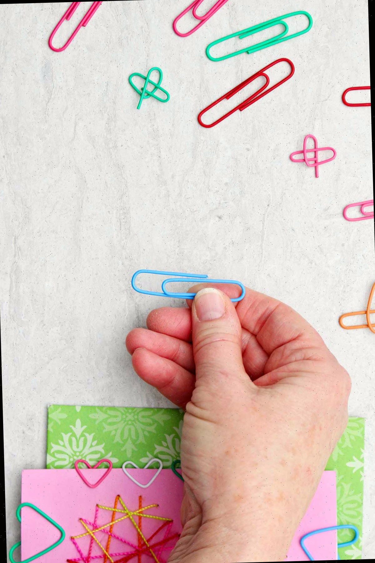 Pessoa segurando um clipe de papel azul com outros clipes de papel e um cartão de Dia dos Namorados próximos.