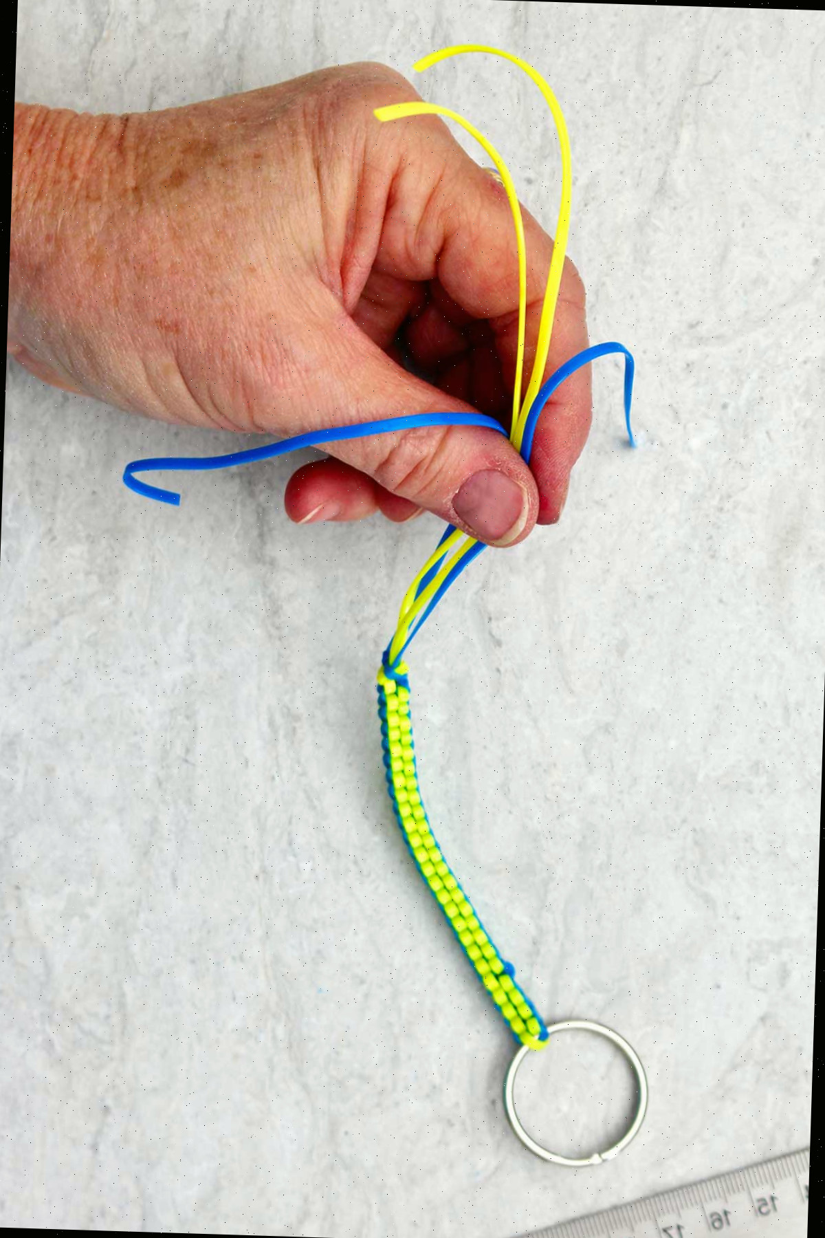 Chaveiro boondoggle azul e amarelo sendo segurado na ponta por uma mão.