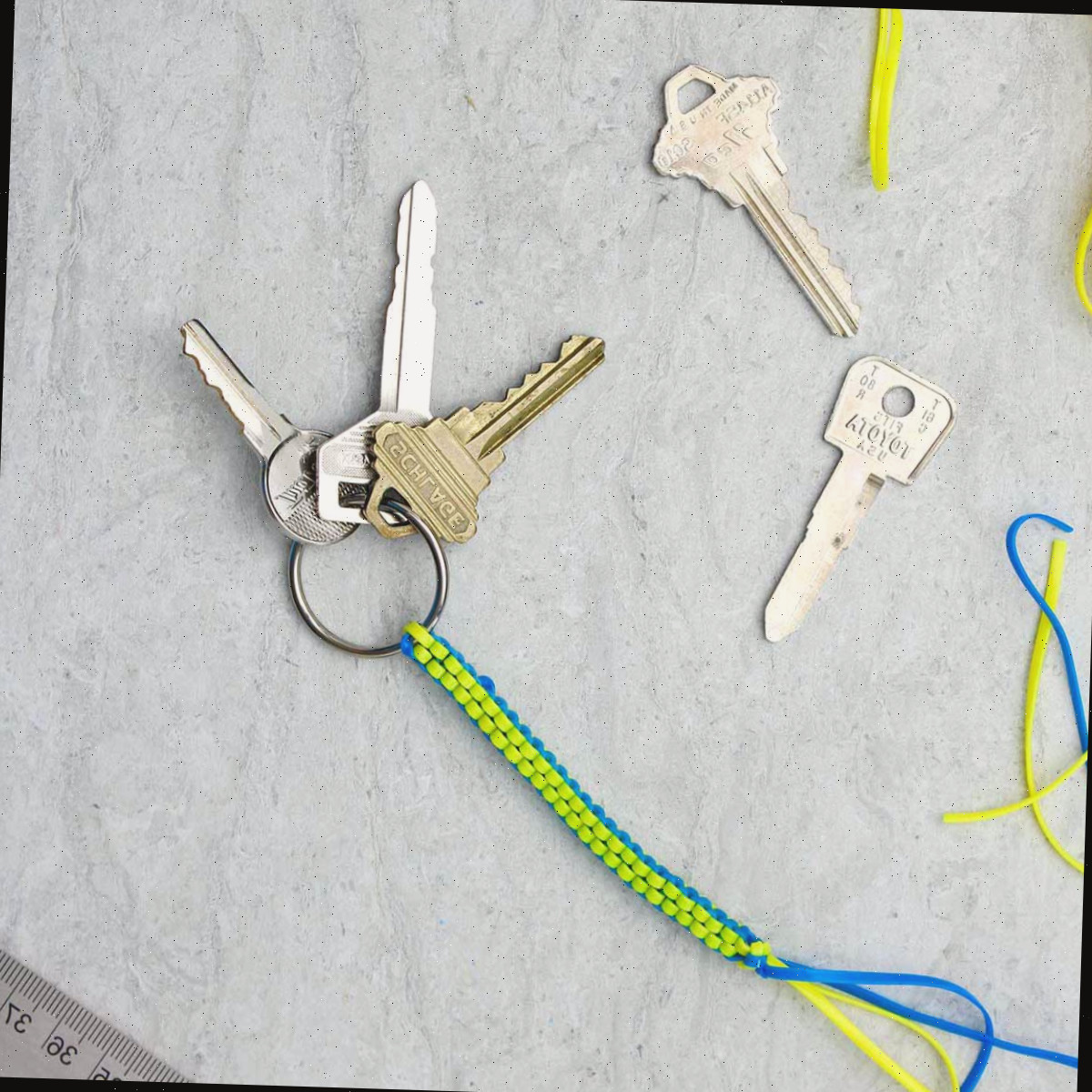 Um chaveiro boondoggle concluído em azul e amarelo com três chaves penduradas e suprimentos próximos.
