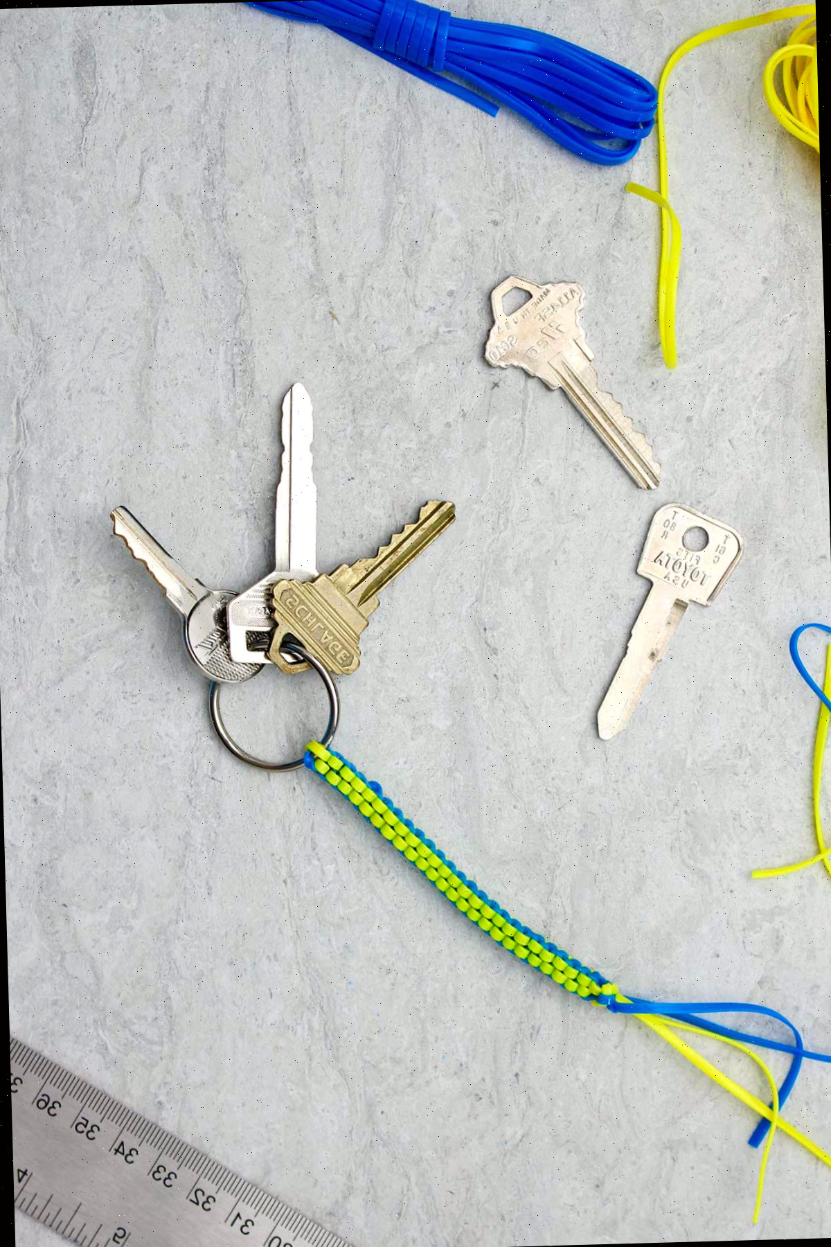 Um chaveiro boondoggle azul e amarelo completo com três chaves anexadas e materiais ao redor.