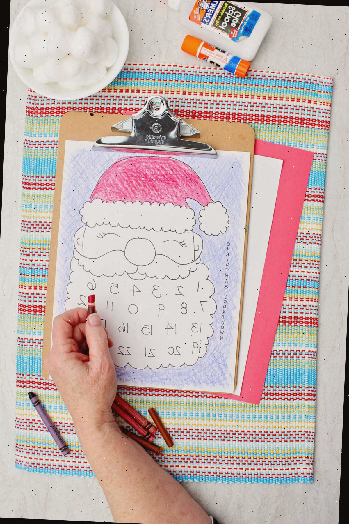 Uma pessoa colorindo o chapéu do Papai Noel de vermelho na impressão do calendário.