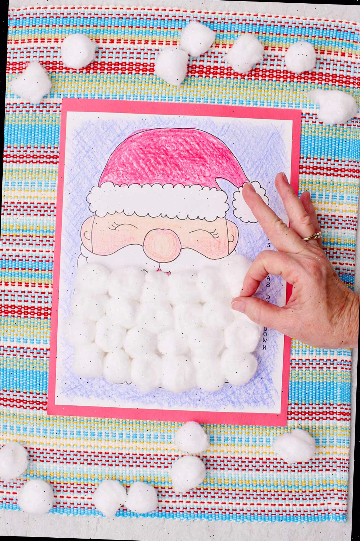 Um calendário de contagem regressiva de Natal completo, colorido com giz de cera e a barba do Papai Noel coberta com bolinhas de algodão e uma pessoa fazendo o sinal de 'ok'.