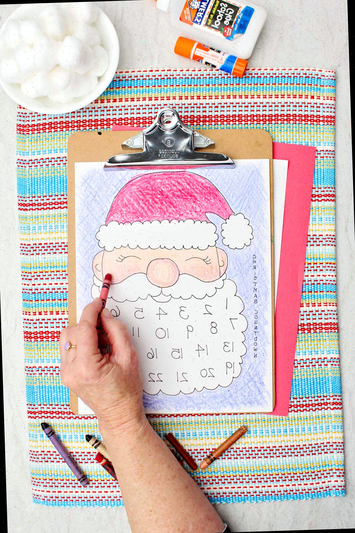 Uma pessoa colorindo as bochechas do Papai Noel de um tom rosado com um lápis de cor vermelho.