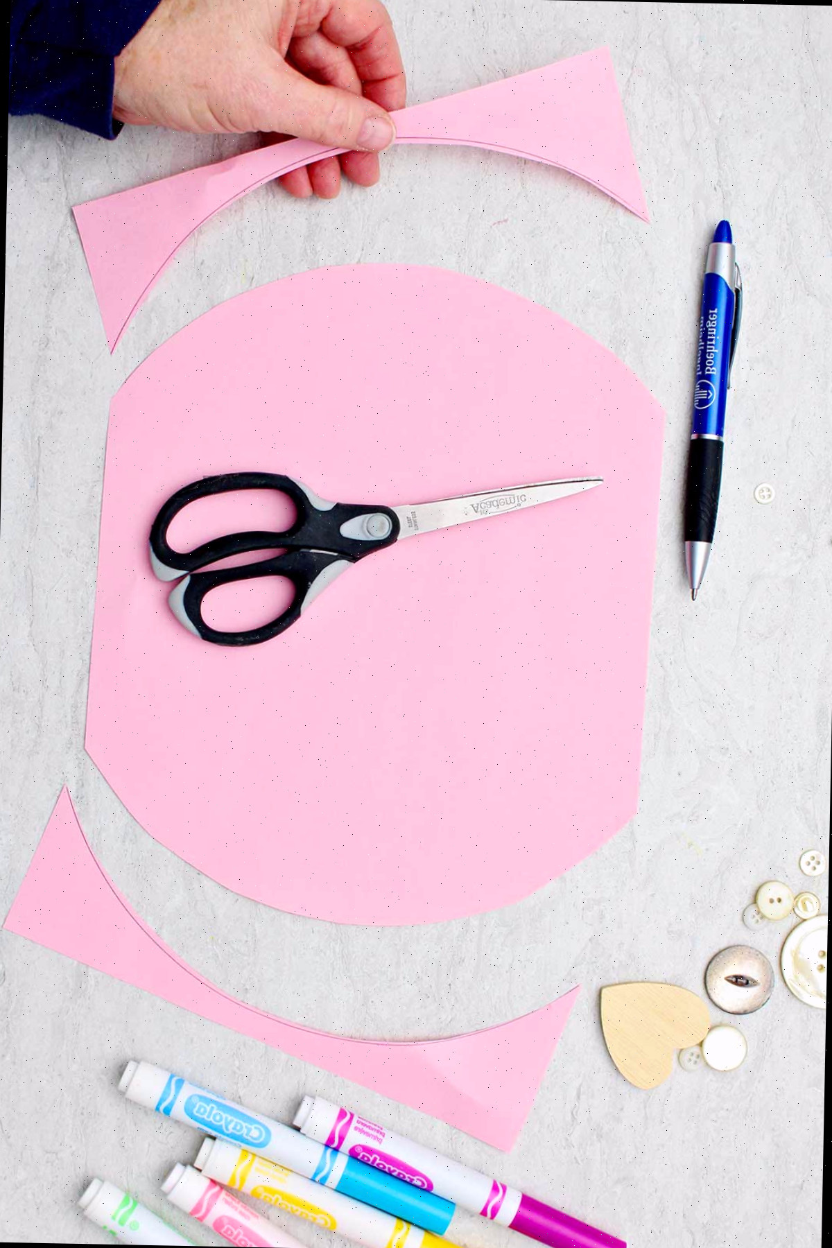 Pessoa cortando um pedaço semicircular de papel rosa claro com as extremidades recortadas para formar um coração de papel em acordeão.