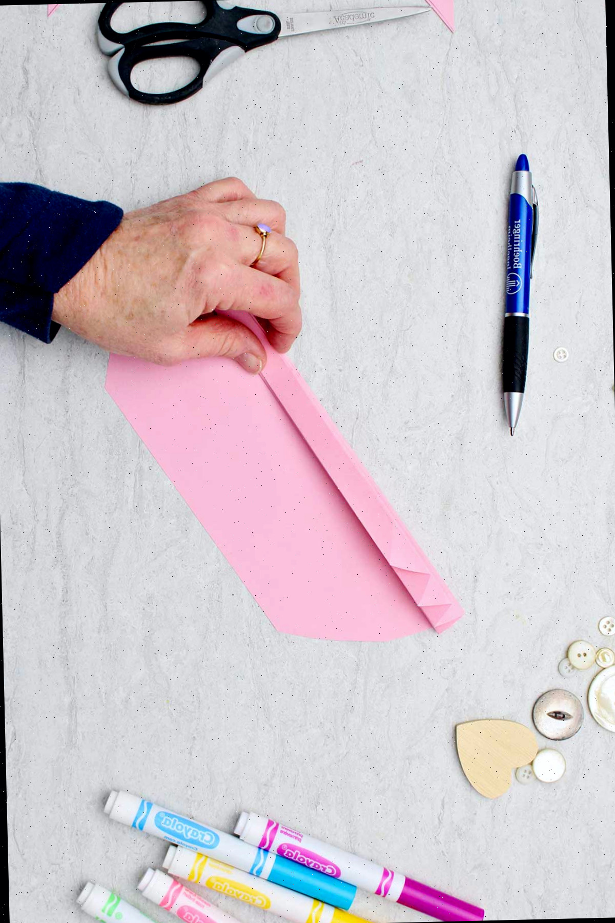 Indivíduo dobrando um pedaço de papel rosa claro para formar um coração de papel em acordeão.