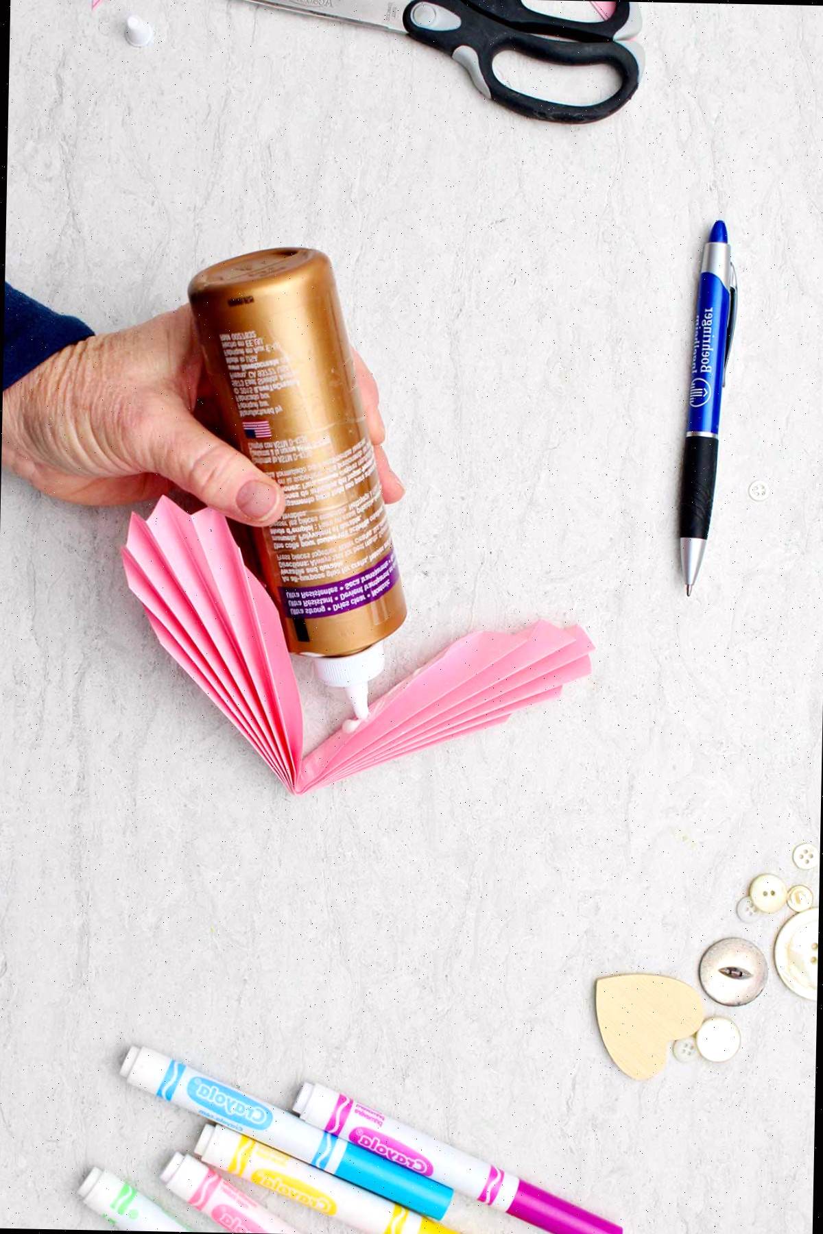 Indivíduo colando a dobra interna de um coração de papel em acordeão.