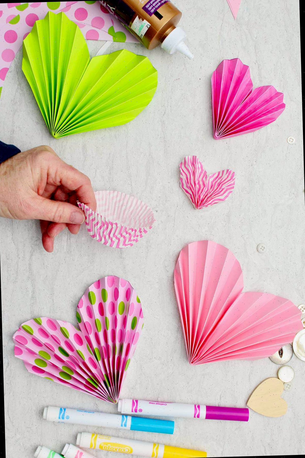 Indivíduo segurando forminhas de cupcake rosa e brancas com outros corações em papel colorido ao redor.