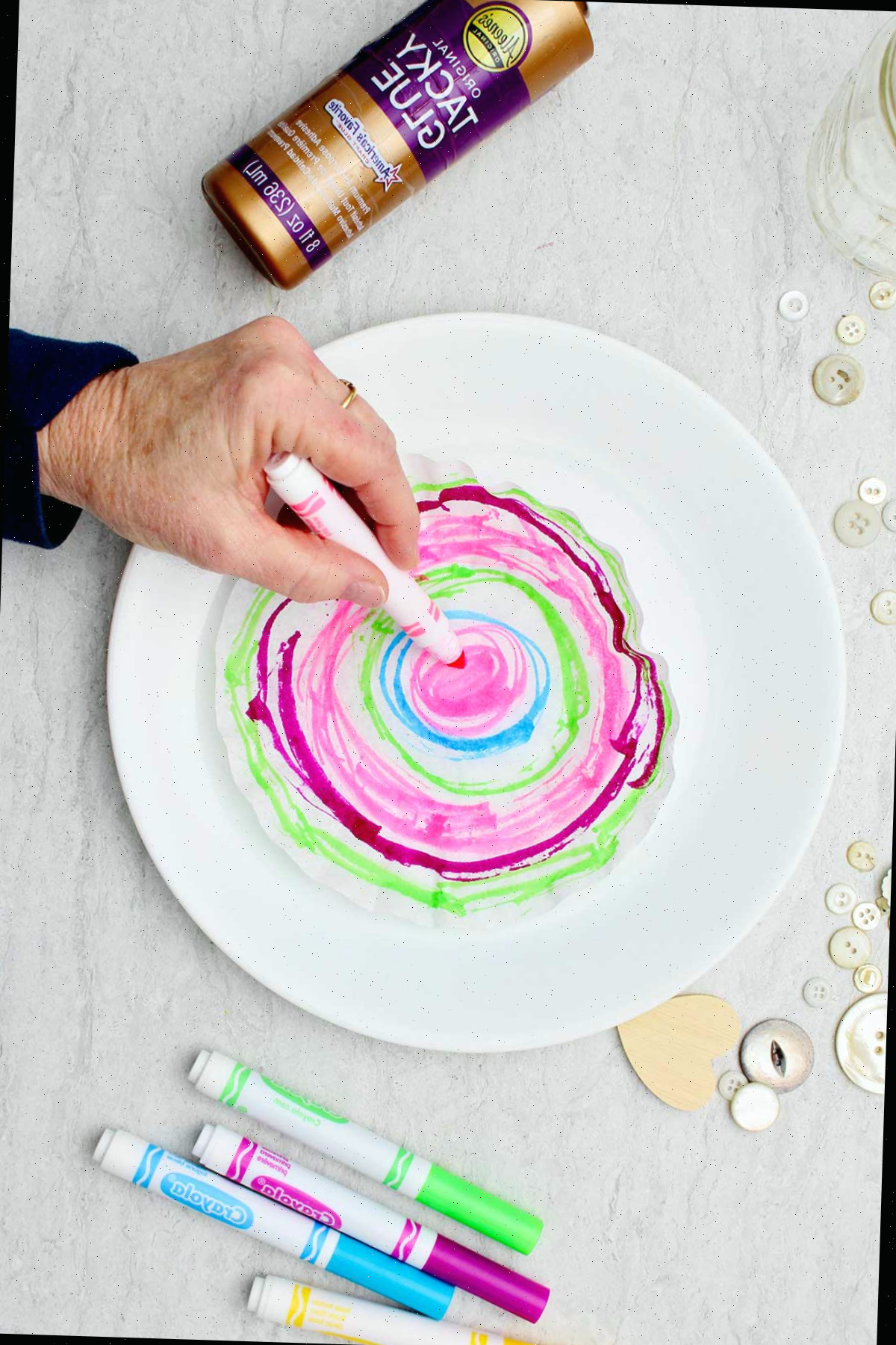 Indivíduo colorindo círculos diferentes com caneta para fazer um coração de papel acordeão tie-dye com outros suprimentos ao redor.