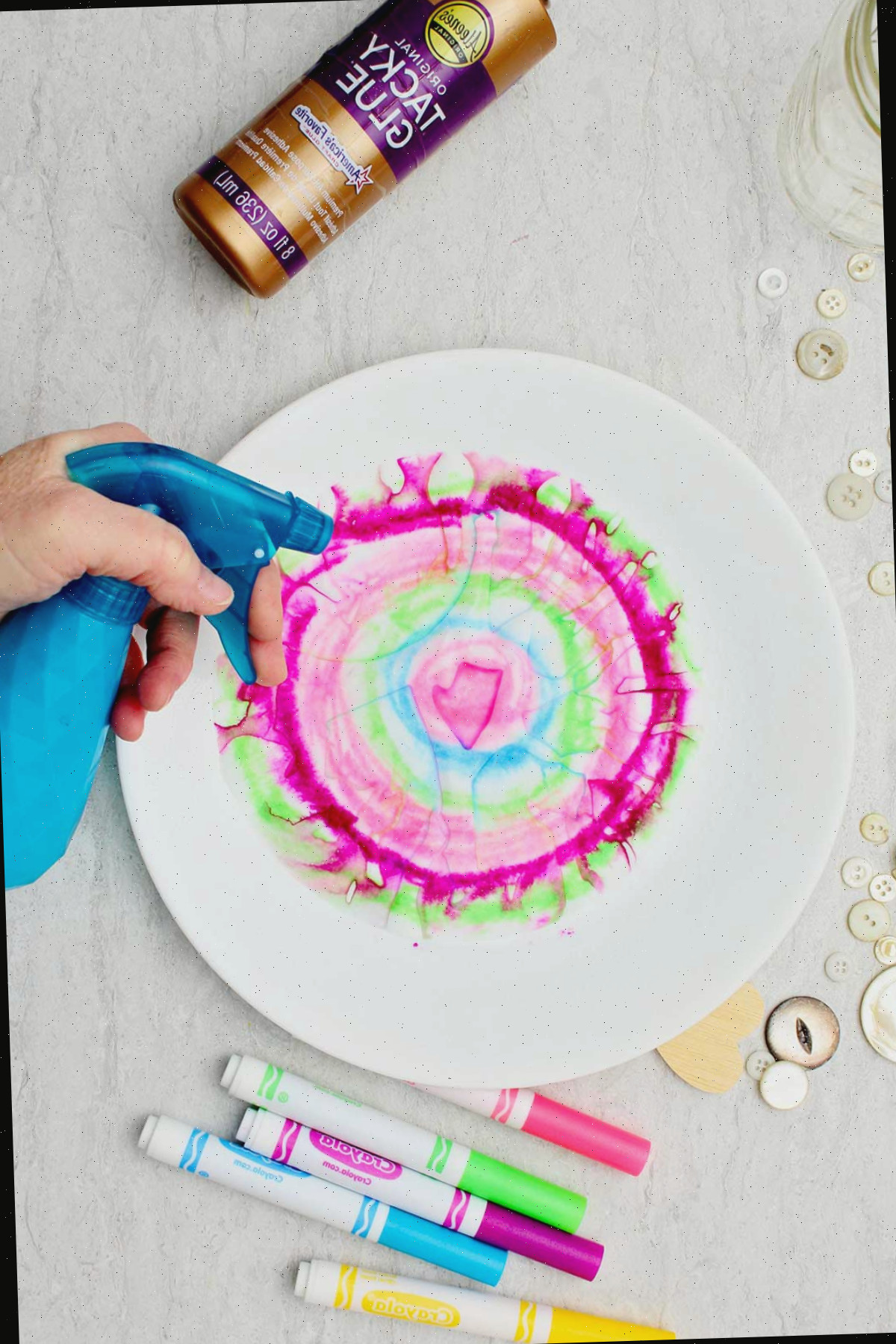 Indivíduo borrifando água em um pedaço circular de papel para fazer um coração de papel acordeão tie-dye.