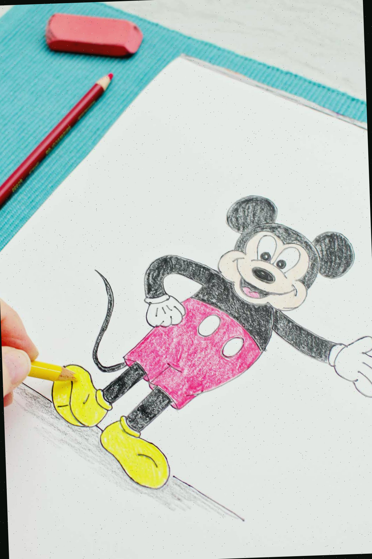 Uma pessoa colorindo os sapatos do Mickey com um lápis de cor amarelo.