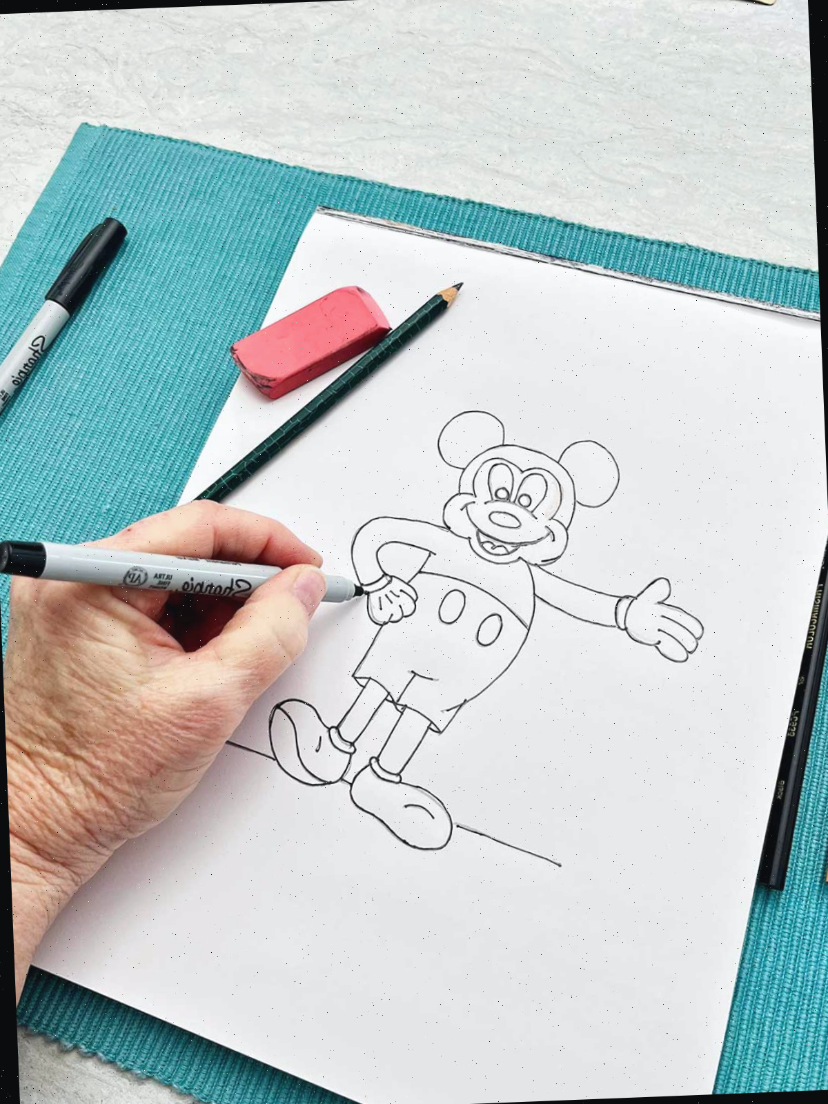 Uma pessoa revisando o esboço a lápis do Mickey Mouse com um marcador sharpie.