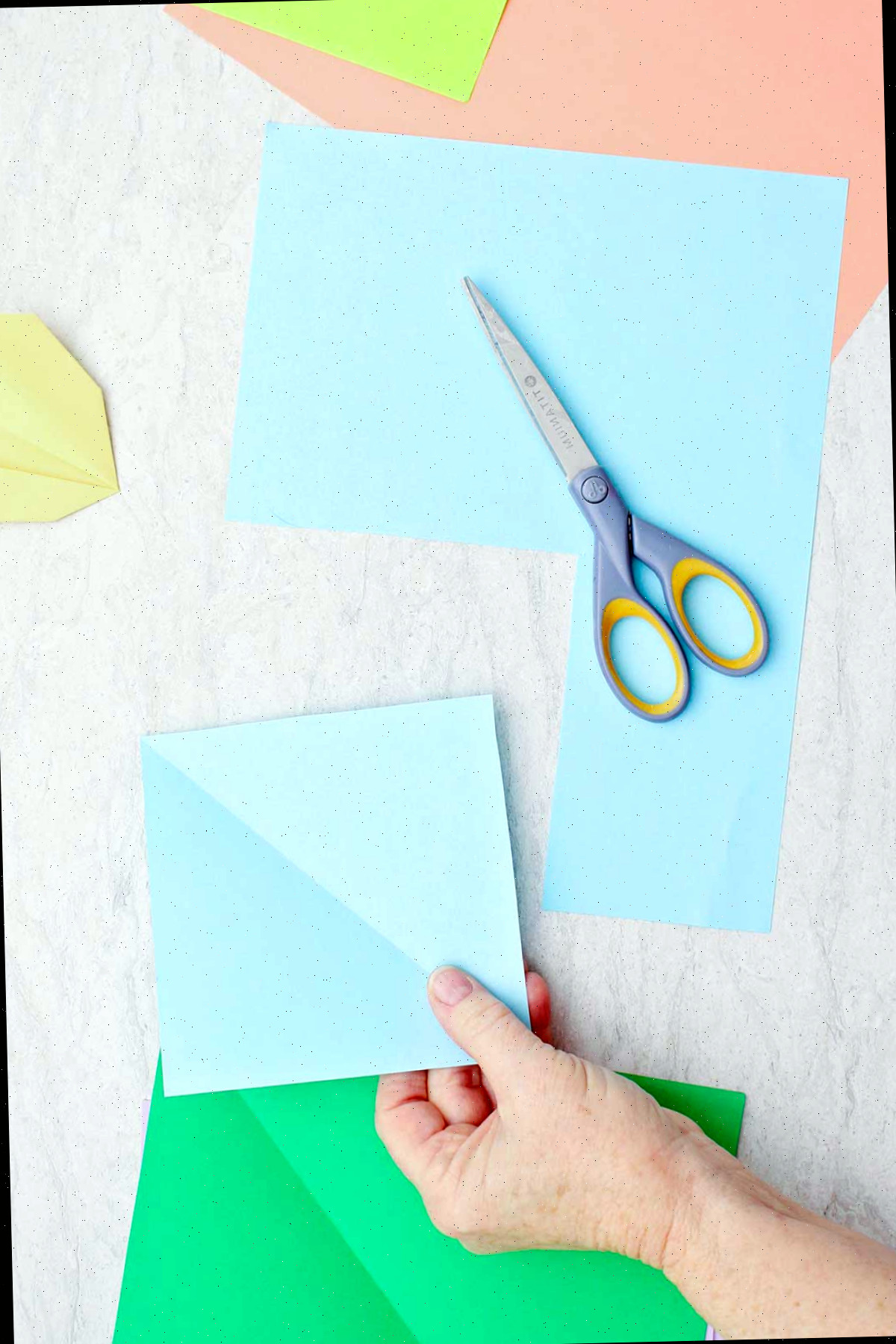 Uma pessoa cortando um quadrado de papel azul claro para fazer uma flor de origami.