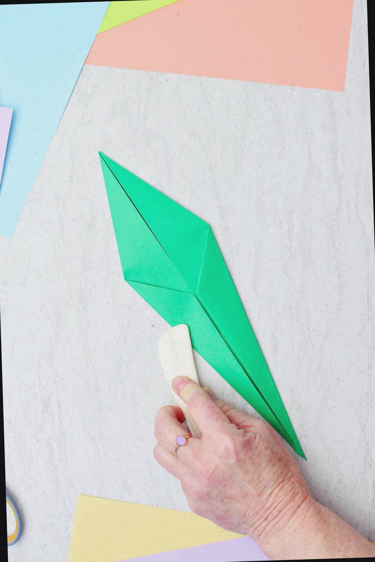 Uma pessoa usando uma espátula de osso para vincar um papel verde para fazer um caule.