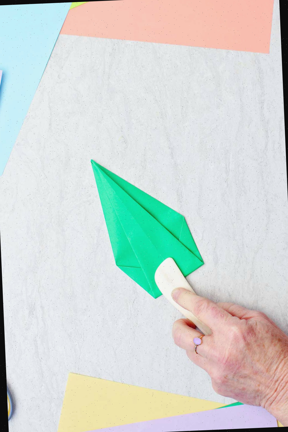 Uma pessoa usando uma espátula de osso para vincar um papel verde para fazer um caule.