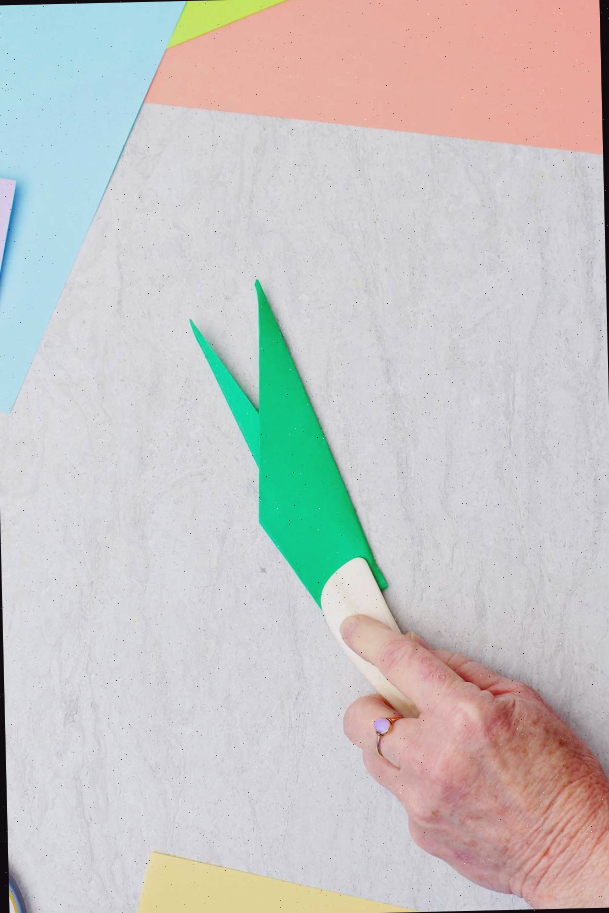 Uma pessoa usando uma espátula de osso para vincar um papel verde para fazer um caule.