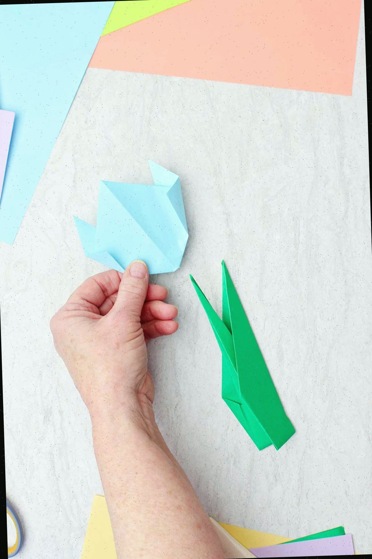 Uma pessoa colocando uma flor de origami azul claro sobre um caule de origami.