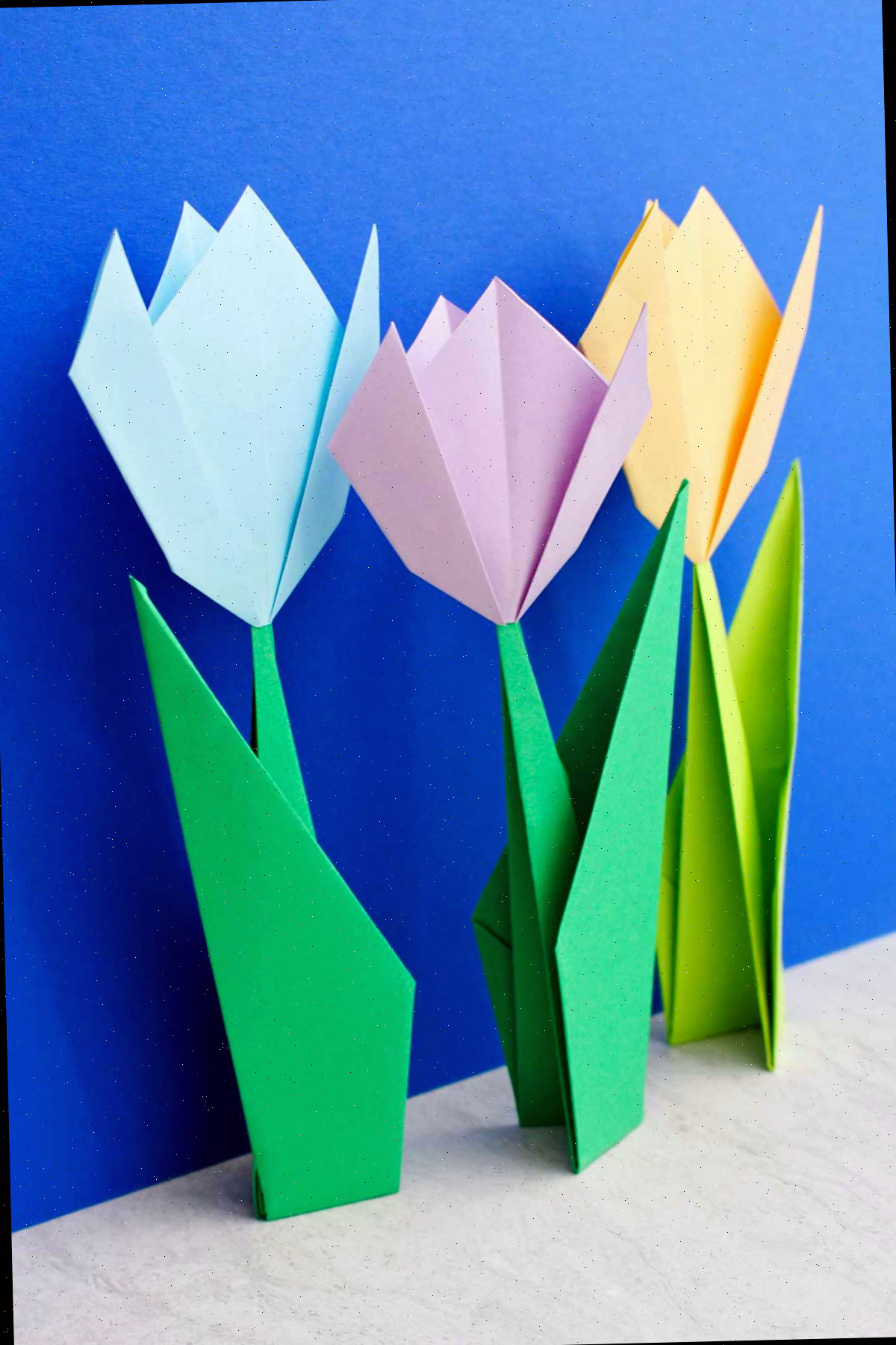 Três flores de origami posicionadas diante de um fundo azul vibrante.