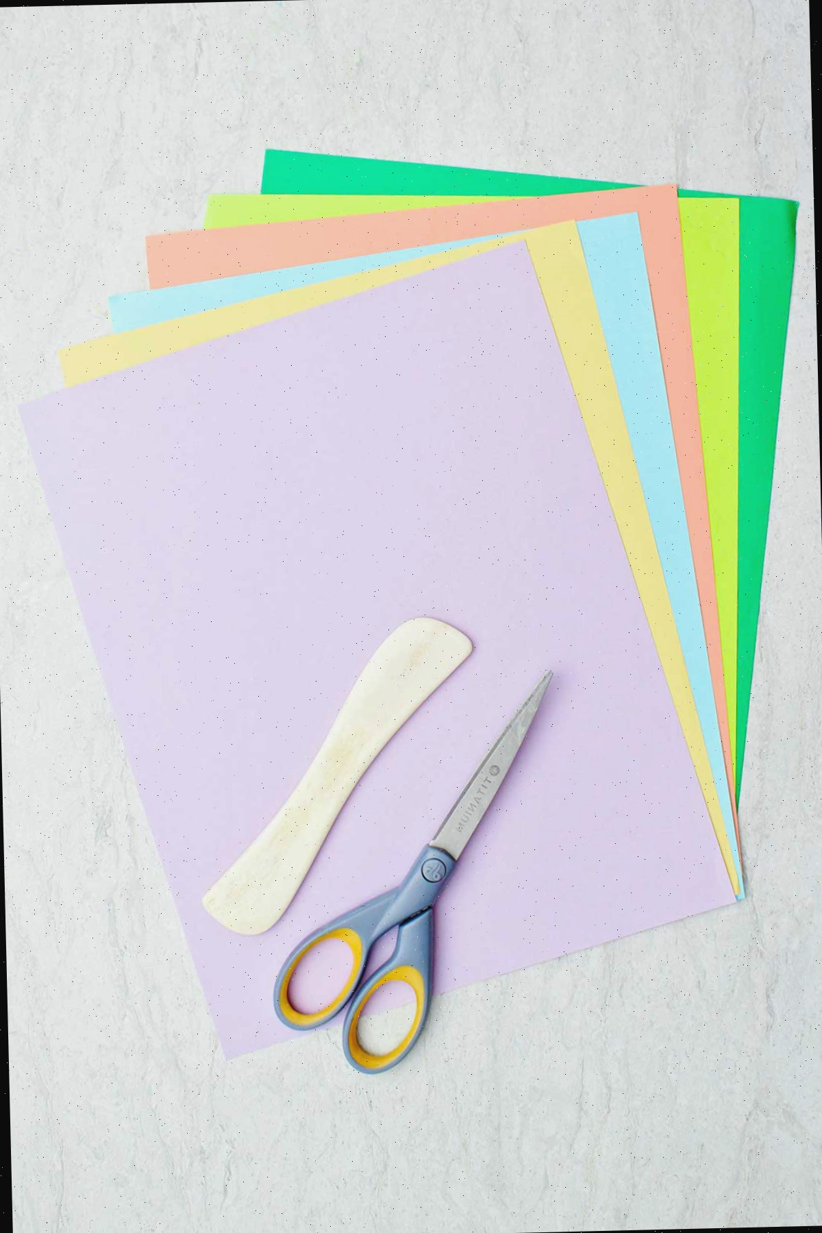 Papel colorido, uma espátula de madeira e tesouras.
